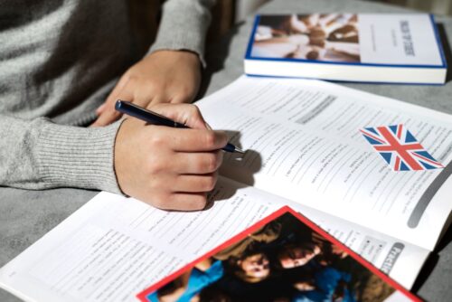 A student filling out an English language workbook with a UK flag sticker on the page, representing preparation for studying in the UK under the updated 2025 visa and immigration rules.