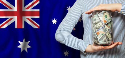 Person holding a jar of US dollar bills in front of the Australian flag, symbolizing rising Australia visa fee 2025 and increased study costs for international students.