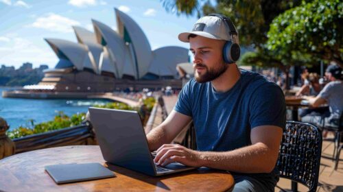 Man wearing headphones working on a laptop outdoors with the Sydney Opera House in the background, symbolizing international student life in Australia 2025.