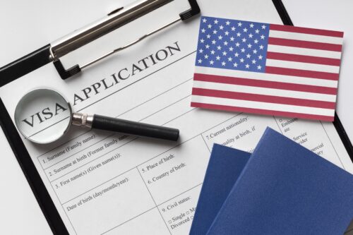 US visa application form with American flag, passport, and magnifying glass – representing the challenges Indian students face with Fall 2025 student visa delays.